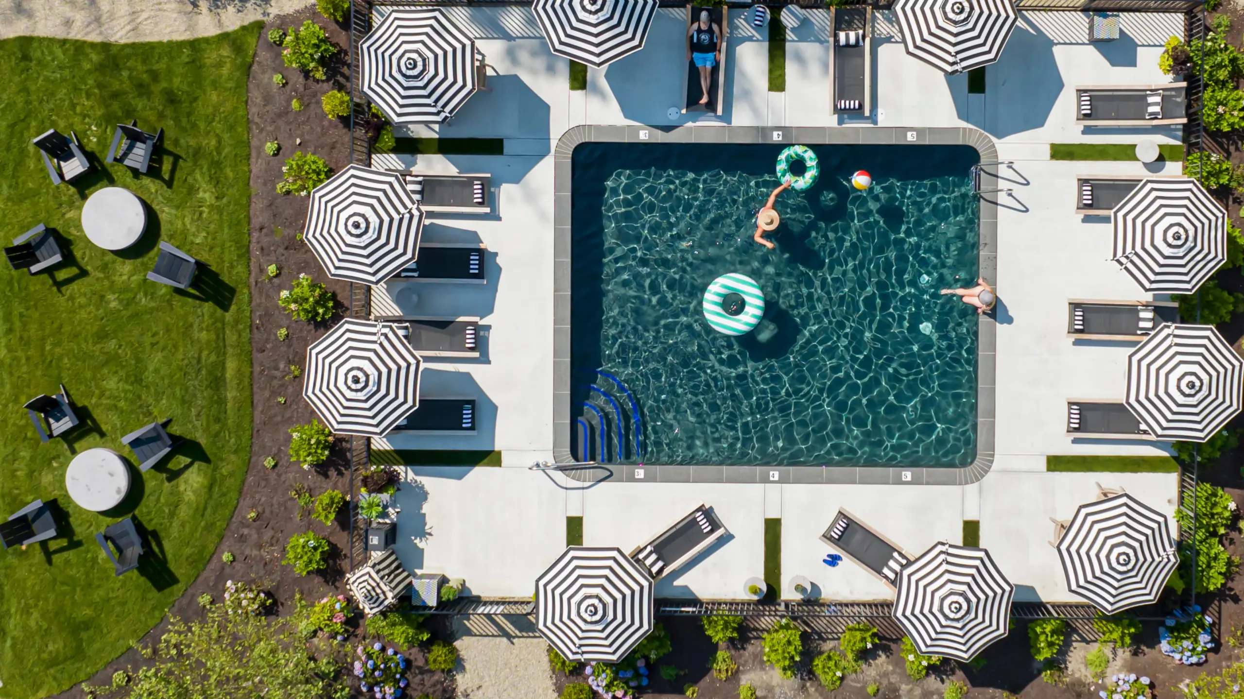 Aerial view of the lounge pool at The Wanderer Cottages in Kennebunk, Maine, lined with striped umbrellas and loungers.